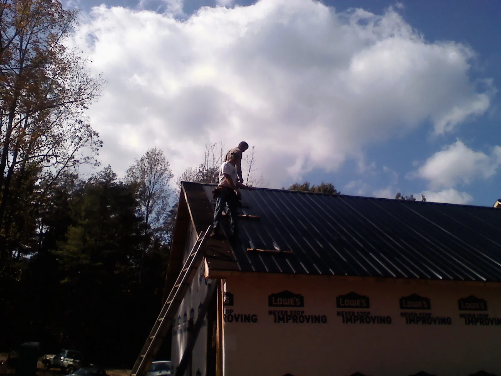 Roofer fastening dark metal panels high against a cloudy sky, from a Roof Inspection job in Woodway