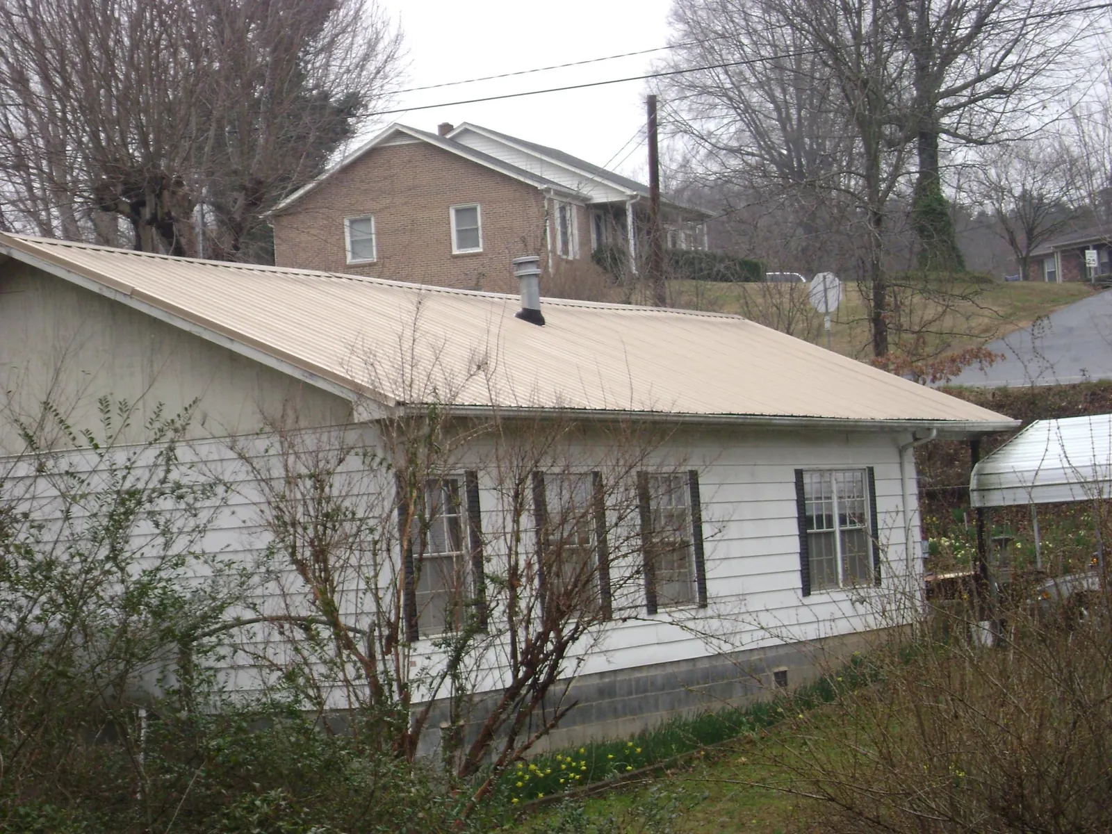 Tan metal roof on a white sided house set into a hillside — Commercial Roofing by Roofing Brothers in Woodway